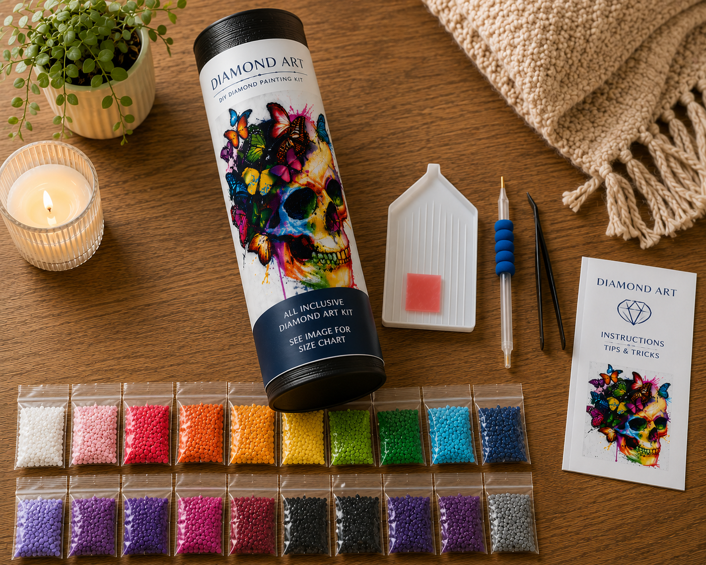 Rainbow Butterfly Skull Diamond Painting Kit – flat lay on warm wood surface showing canvas rolled in a Diamond Art tube labeled "All Inclusive Diamond Art Kit", 20 resealable diamond drill bags in a full rainbow spectrum including white, pink, red, orange, yellow, green, teal, blue, purple, and black, white grooved sorting tray, blue applicator pen, black tweezers, pink wax pad, and Diamond Art instructions booklet beside a glowing candle and trailing plant