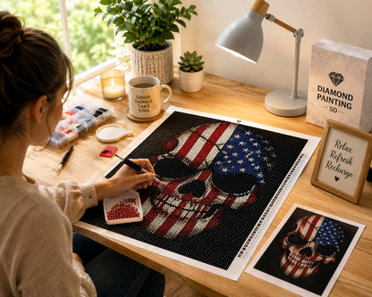  Woman creating American flag skull Stars &amp; Stripes Skull Diamond Painting Kit – woman placing diamond drills on large stars and stripes skull canvas at bright wood desk with diamond organizer box, red sorting tray, applicator pen, red wax pad, "Good Things Take Time" mug, candle, potted plants, desk lamp, "Diamond Painting 5D" sign, "Relax Refresh Recharge" sign, and reference print in natural daylight
