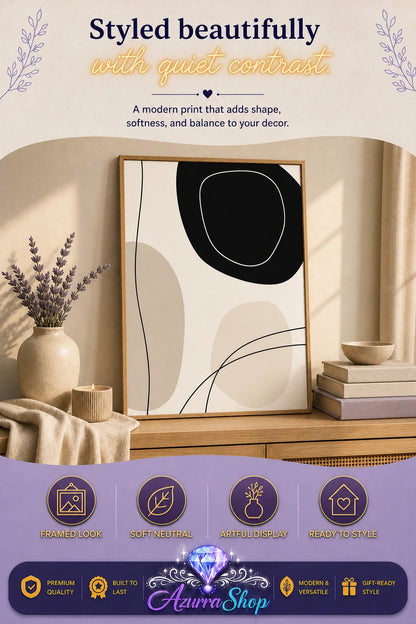 Framed abstract canvas print with black and beige organic shapes leaning against a wall on a wooden console table with a lit candle, stacked books, a small bowl, and a curtain in the background