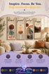 Four vertical wooden wall art panels reading "blessed," "focused," "grateful," and "happy" in black script, each with an abstract earth-toned pattern, displayed on a wall above a beige sofa with cream pillows and a potted plant.
