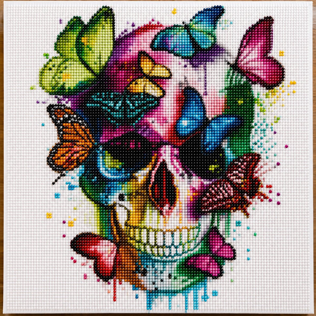 Close up of the finished colorful sugar skull diamond painting covered in rainbow butterflies on a white canvas | Azurra Shop