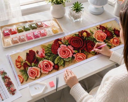 Woman placing diamonds on the crimson rose garland canvas at a desk by a window | Azurra Shop