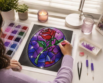 Woman placing diamonds on the stained glass rose canvas at a desk by a sunny window | Azurra Shop